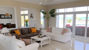A spacious living room with two white sofas, a brown sofa, and a coffee table. There is a large window with a view of the ocean.