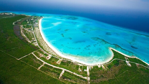 An aerial view of a coastal area with a beach, clear blue waters, and green vegetation.