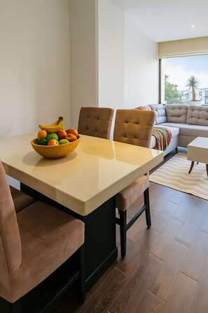 A modern dining area with a wooden table, cushioned chairs, and a fruit bowl. - La Silla View Luxury Penthouse Pool and Gym Access (Monterrey)