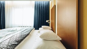 Habitación de hotel con cama, cabecera de madera, ventana con cortinas y lámpara de noche.