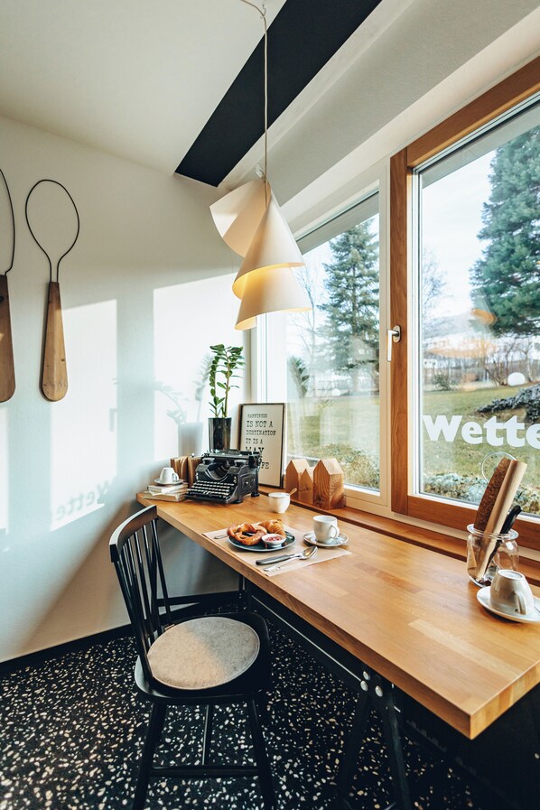 Un comedor moderno con una mesa de madera, una silla negra, una lámpara colgante y una ventana con vistas a la vegetación.