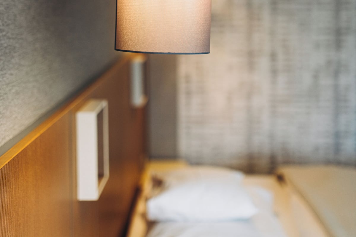 A hotel room with a bed, a nightstand, and a wall-mounted lamp.