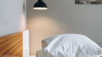 Een net opgemaakt bed met witte lakens, een houten hoofdbord, een hangende吊灯 en een lijst met een afbeelding aan de muur.
