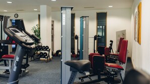 Un gimnasio con equipamiento de ejercicio, estantes para pesas y sillas rojas.