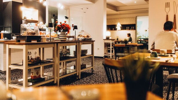 Un moderno comedor con una isla central, mesas, sillas y una cocina al fondo.