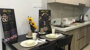 Une cuisine moderne avec une table à manger pour deux, agrémentée d’un tableau affichant le menu, d’un vase avec des tournesols et d’une bouilloire posée sur le plan de travail.