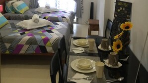 Une chambre d’hôtel avec deux lits, une table à manger dressée pour deux personnes et une vue sur l’extérieur par la fenêtre.