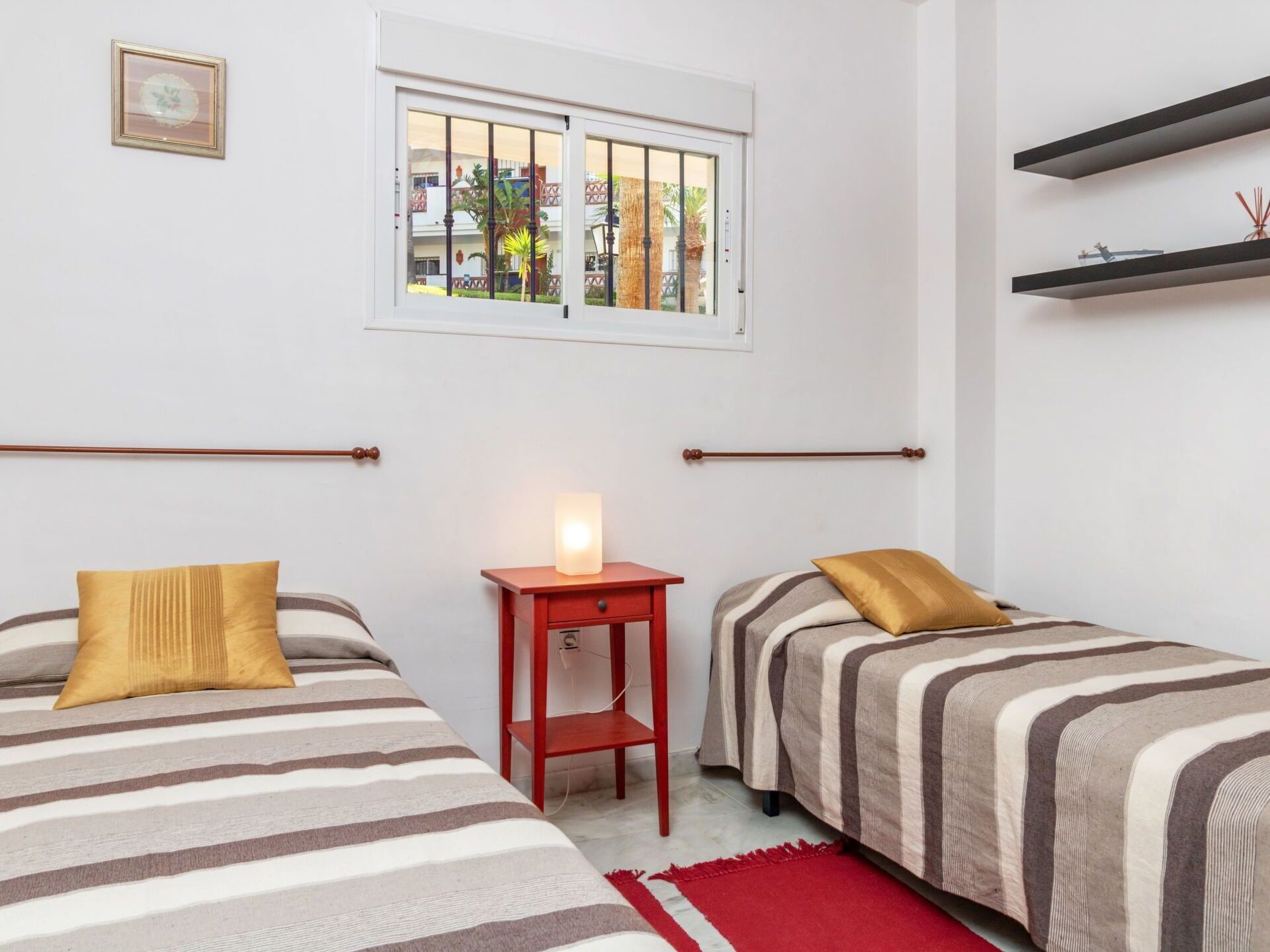 Une chambre avec deux lits, une fenêtre, une table de chevet avec une lampe et un tapis rouge.