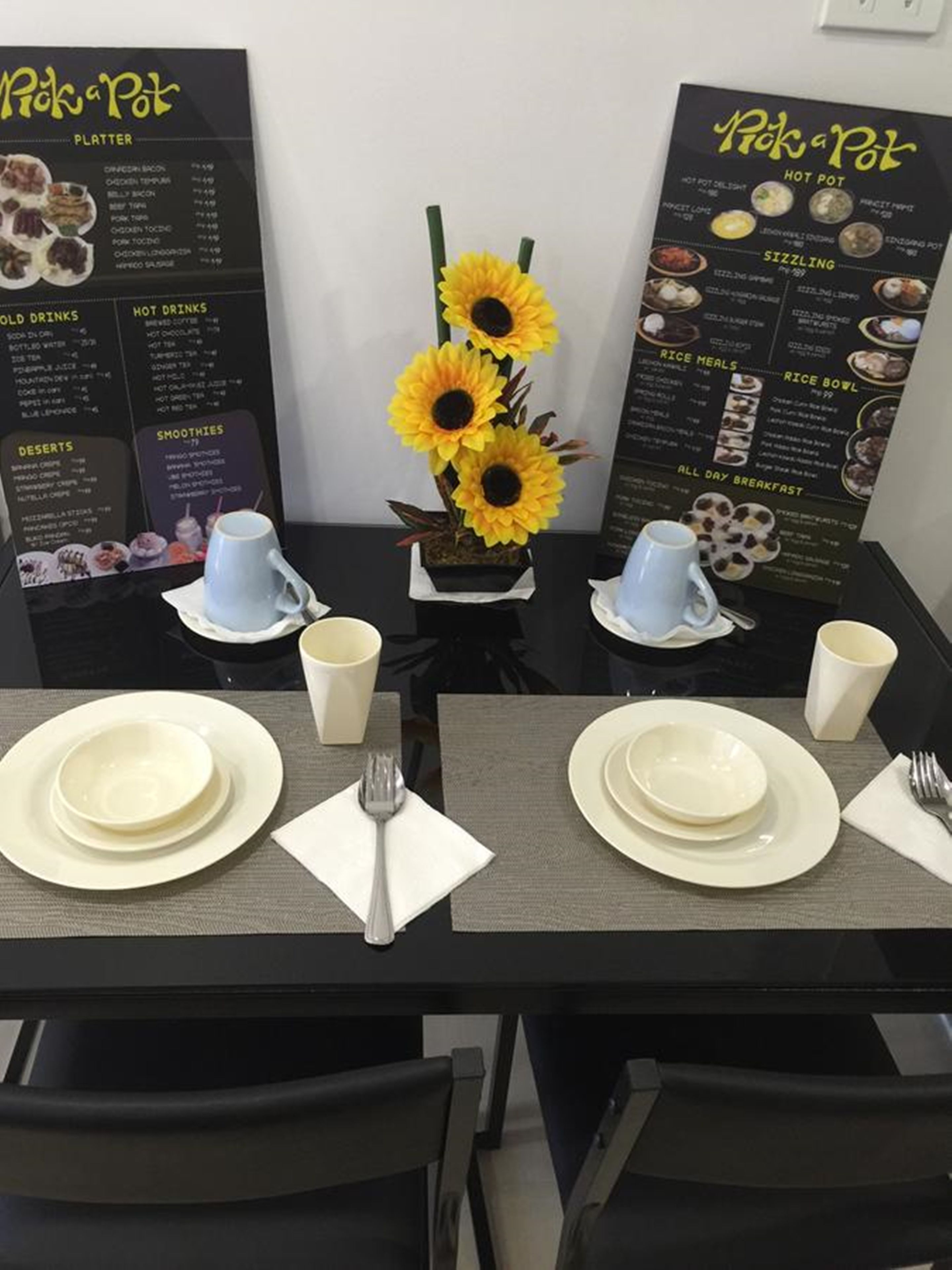 A dining table set with white plates, cups, and cutlery, flanked by two menus for 'Pick a Pot' restaurant.