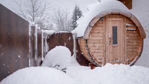 En træhytte med en rund dør, omgivet af snedækket jord og et træstakværk.