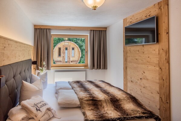 A bedroom with a bed, a window with curtains, a wooden headboard, and a mounted TV. - Viktoria Lodges (Bach)