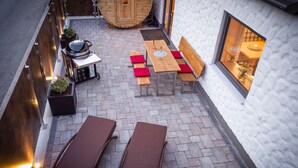 En udendørs terrasse med et træbord og bænke, en sauna og et vindue med blomster.