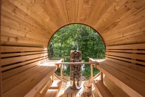 A wooden cabin with a circular window, a central fire pit, and a wooden bench. - Viktoria Lodges (Bach)