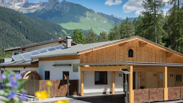 A wooden cabin with a covered porch, solar panels, and a mountain backdrop. - Viktoria Lodges (Bach)