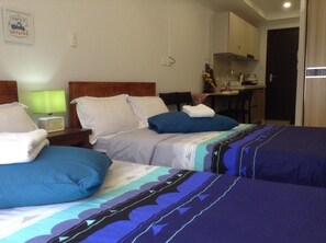 A hotel room with two beds, a small kitchenette, and a dining area.