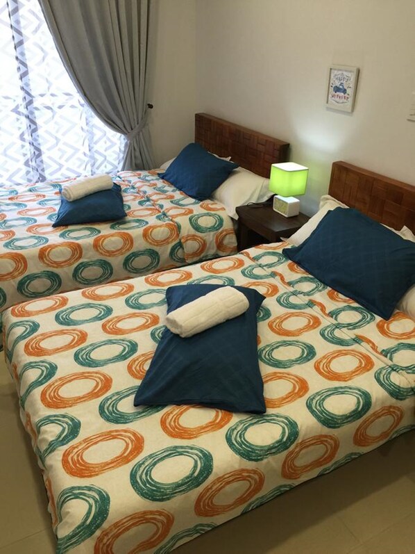 Una habitación de hotel con dos camas, cada una con una colcha estampada, almohadas y una mesita de noche con lámpara.