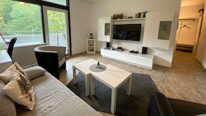 A modern living room with a sofa, coffee table, TV, and speakers. - DeLuchs bed linen bookable - DeLuchs (Bad Harzburg)