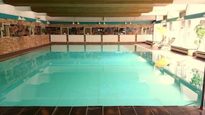 A swimming pool with a tiled floor, surrounded by walls with a brick pattern and mirrored panels.