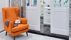 A modern interior with a marble wall, a white door with glass panels, and an orange armchair with a handbag. - Exquisite Pool Villa C (Pattaya)