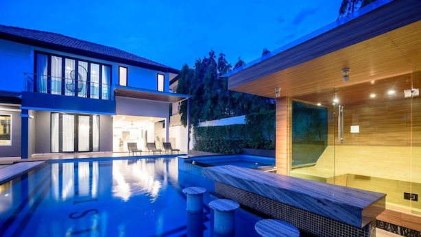 A modern house with a swimming pool, a glass-enclosed spa area, and a well-lit outdoor seating area. - Exquisite Pool Villa C (Pattaya)
