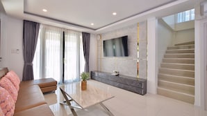 A modern living room with a sofa, a coffee table, a TV mounted on the wall, and a staircase. - Exquisite Pool Villa C (Pattaya)