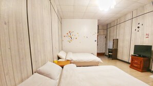 Quarto de hotel com duas camas, um guarda-roupa de madeira, uma televisão e uma parede com adesivo floral.