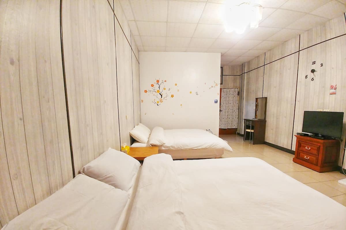 A hotel room with two beds, a wooden wardrobe, a television, and a wall with a floral decal.
