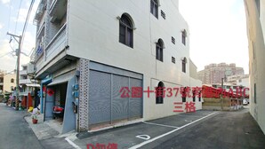 Um edifício com uma persiana fechada no andar térreo, uma varanda no segundo andar e uma placa com letras vermelhas.