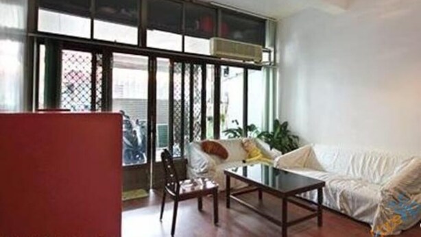 Uma sala de estar moderna com um sofá, uma mesa de centro e uma poltrona. Há uma janela grande com persianas e um lustre.