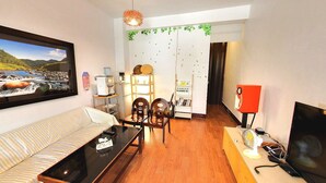 Uma sala de estar com sofá, mesa de jantar, cadeiras, televisão e estante de livros.