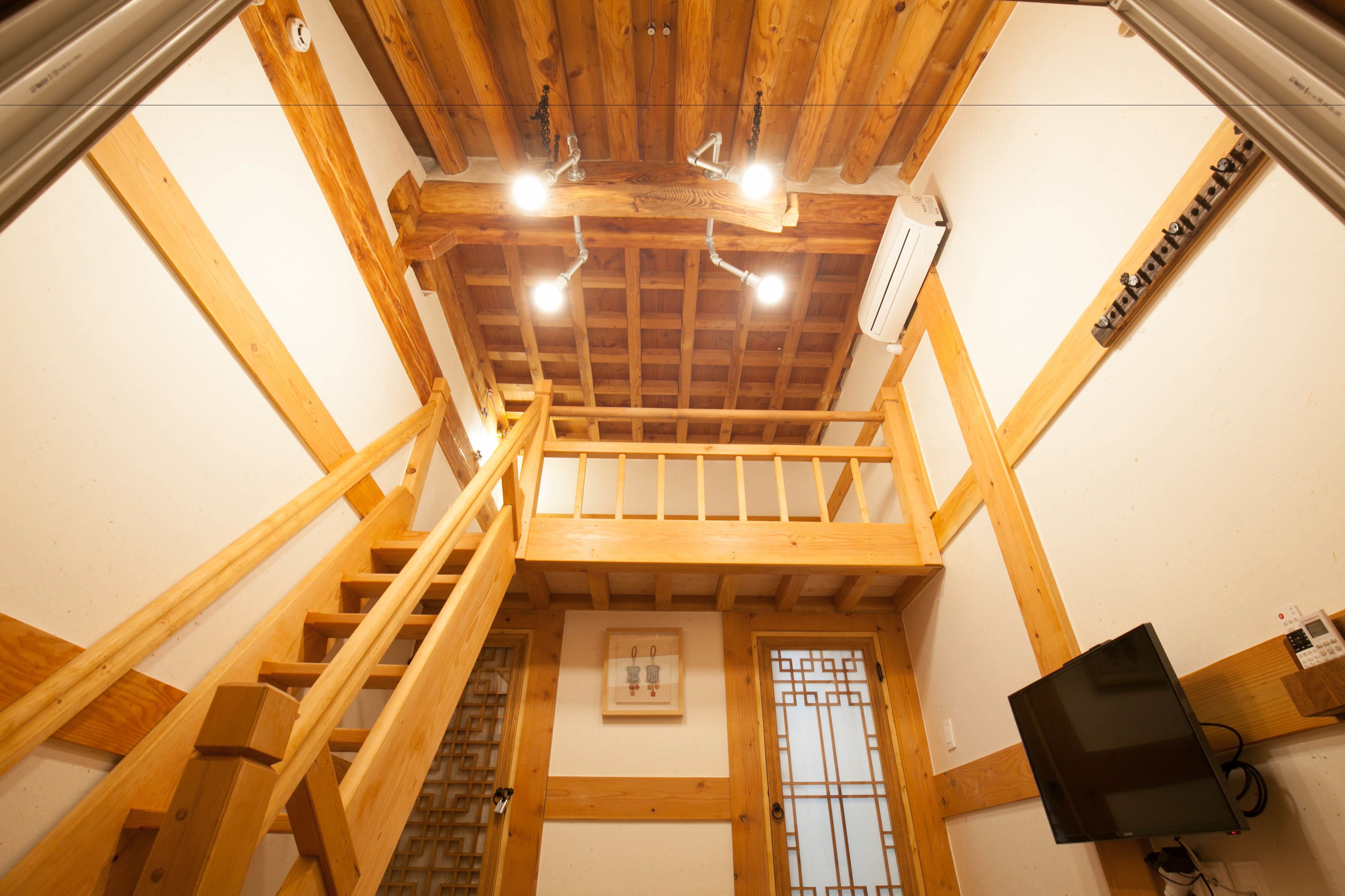 A wooden staircase leading to a loft area with a ceiling fan, a framed picture on the wall, and a television mounted on the wall.