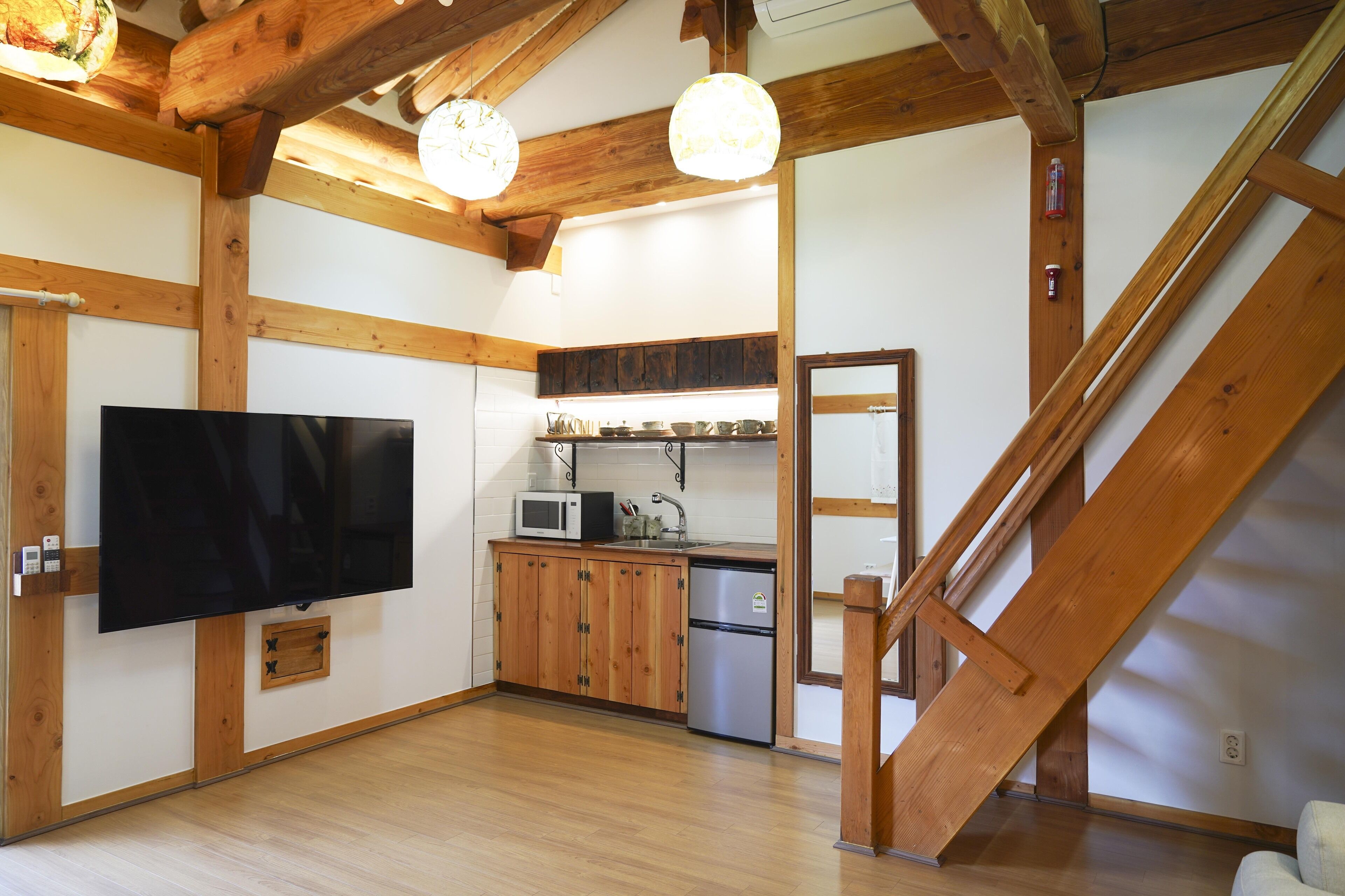 A kitchen with wooden beams, a flat-screen TV, a microwave, and a refrigerator.