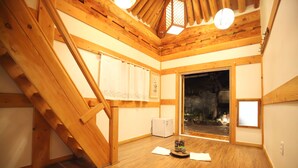 A room with wooden beams, a staircase, a small table with a decorative item, and a view through a door. - Samlockhon (Jeonju)