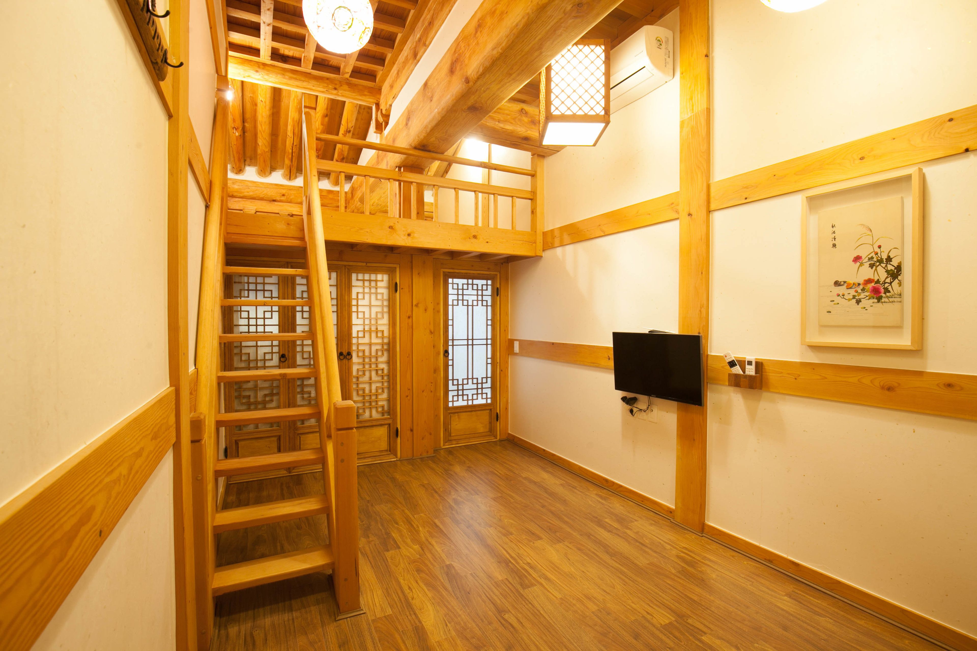 A wooden interior with a wooden staircase, a door with a geometric pattern, and a framed artwork on the wall.