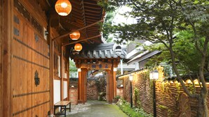 A traditional wooden building with a covered walkway, stone flooring, and a bench. - Samlockhon (Jeonju)