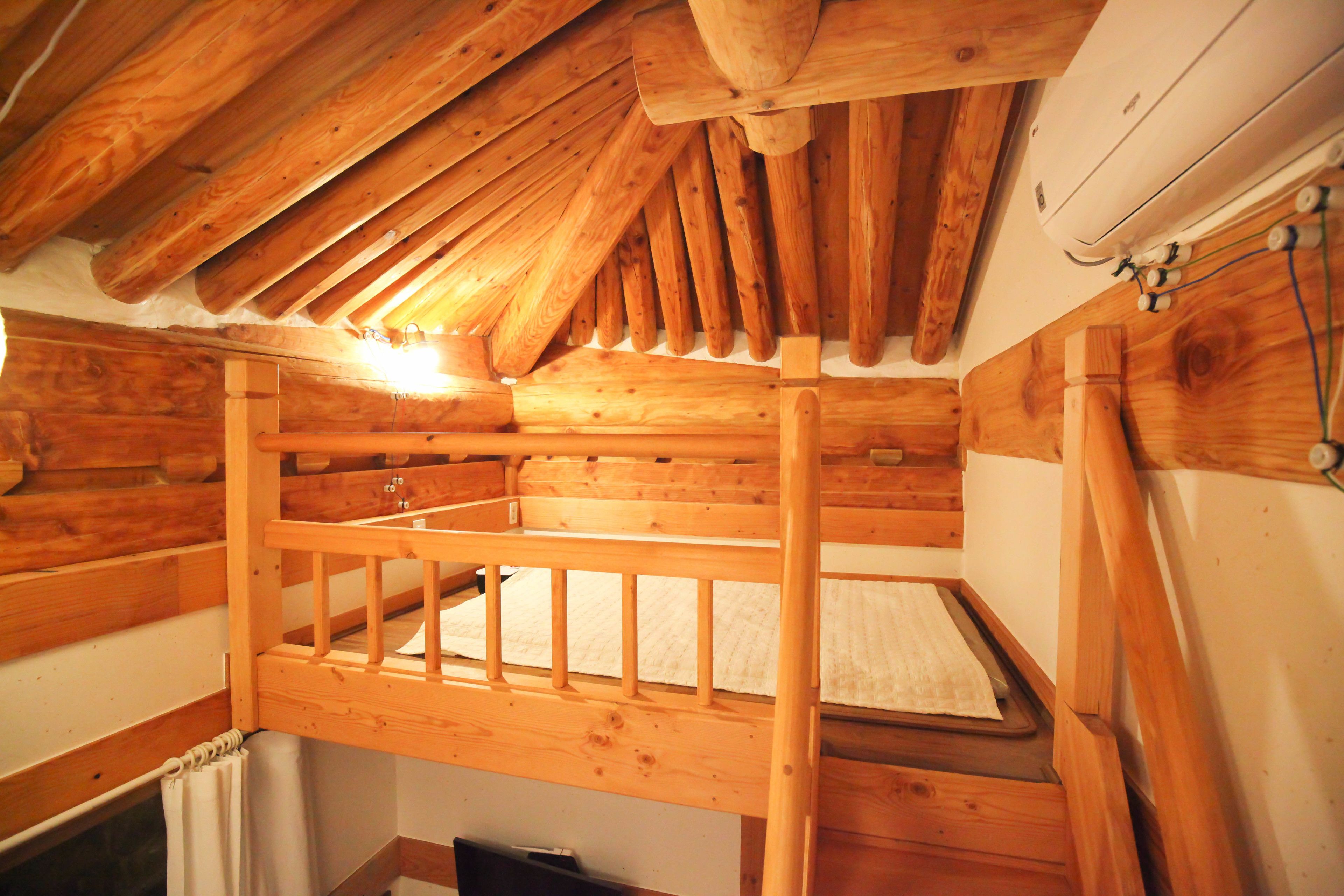 Una cama nido de madera en una habitación de estilo cabaña, con techo inclinado y un equipo de aire acondicionado blanco en la pared.