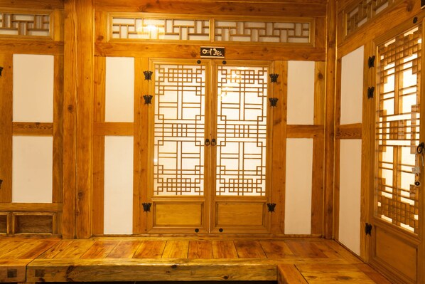 A traditional wooden room with a central door featuring intricate lattice designs and a wooden bench in the foreground. - Samlockhon (Jeonju)