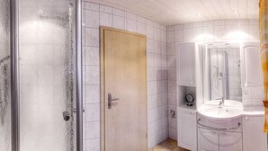 Un baño con azulejos blancos, una puerta de madera, un lavabo con espejo y una zona de ducha.