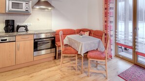 Una cocina compacta con electrodomésticos modernos, un comedor con mesa y sillas, y un gran ventanal con cortinas.