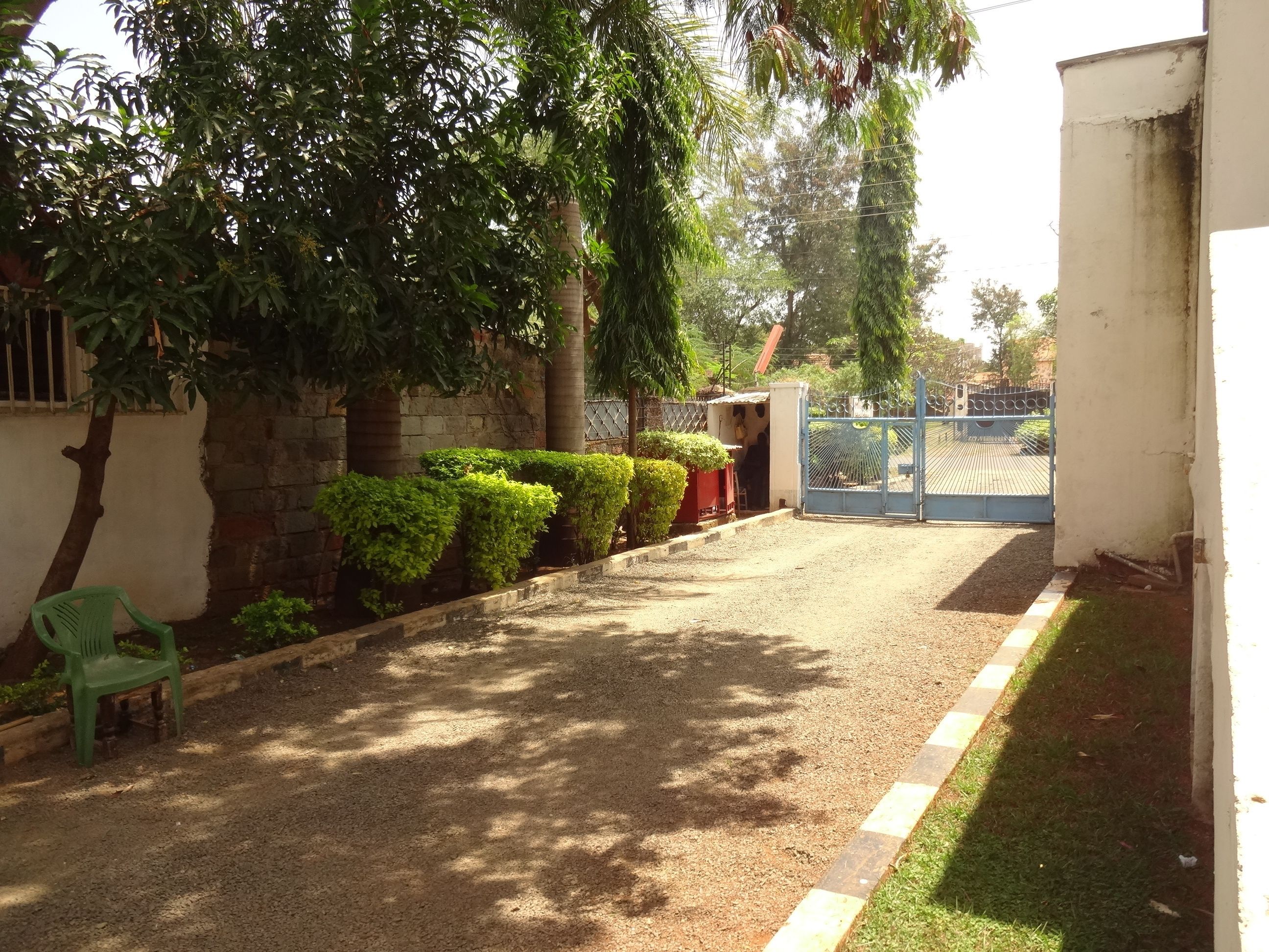 A gravel driveway leading to a gated entrance, surrounded by neatly trimmed hedges and trees.