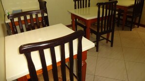 A dining area with wooden tables and chairs, a tiled floor, and a plain wall. - Milimani Holiday Resort (Kisumu)