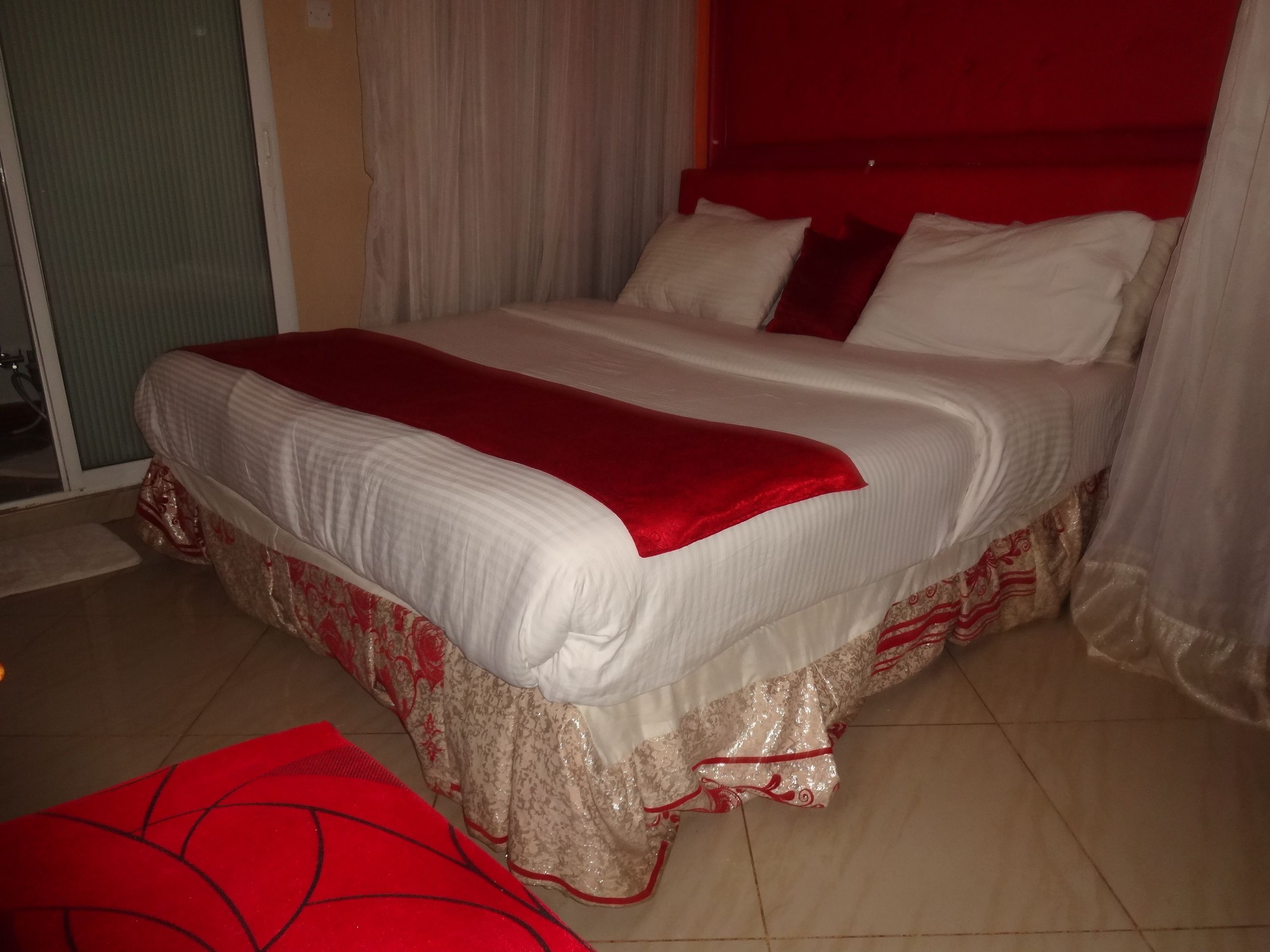 Un lit bien fait, recouvert d’une couvre-lit rouge et blanche, agrémenté d’un plaid rouge et d’une housse décorative au pied du lit.