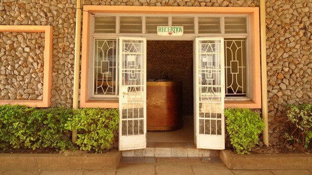 A reception area with a stone wall, a reception desk, and a sign that reads "RECEPTION". - Milimani Holiday Resort (Kisumu)
