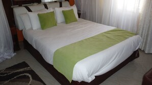 A hotel room with a large bed, a TV mounted on the wall, and a wooden headboard. - Milimani Holiday Resort (Kisumu)