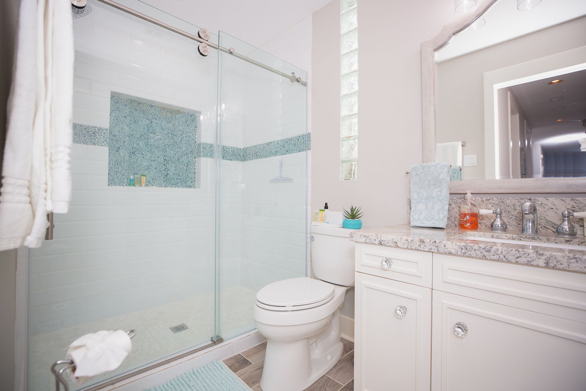 A modern bathroom with a glass-enclosed shower, a white toilet, and a marble countertop with a sink and mirror.