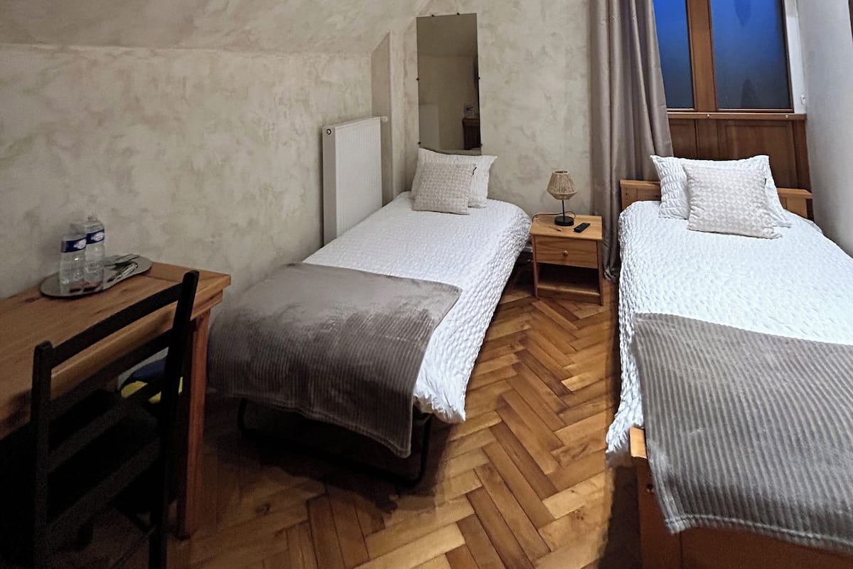 Une chambre avec deux lits, un bureau, une chaise, une petite table, un miroir et une fenêtre de toit.