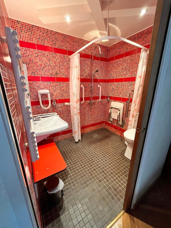 Un baño con zona de ducha con azulejos rojos, un lavabo blanco y un inodoro.