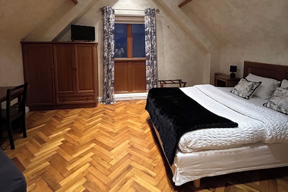 Une chambre avec un parquet en chevrons, un lit avec une literie blanche, un téléviseur posé sur un meuble en bois et des fenêtres de toit.