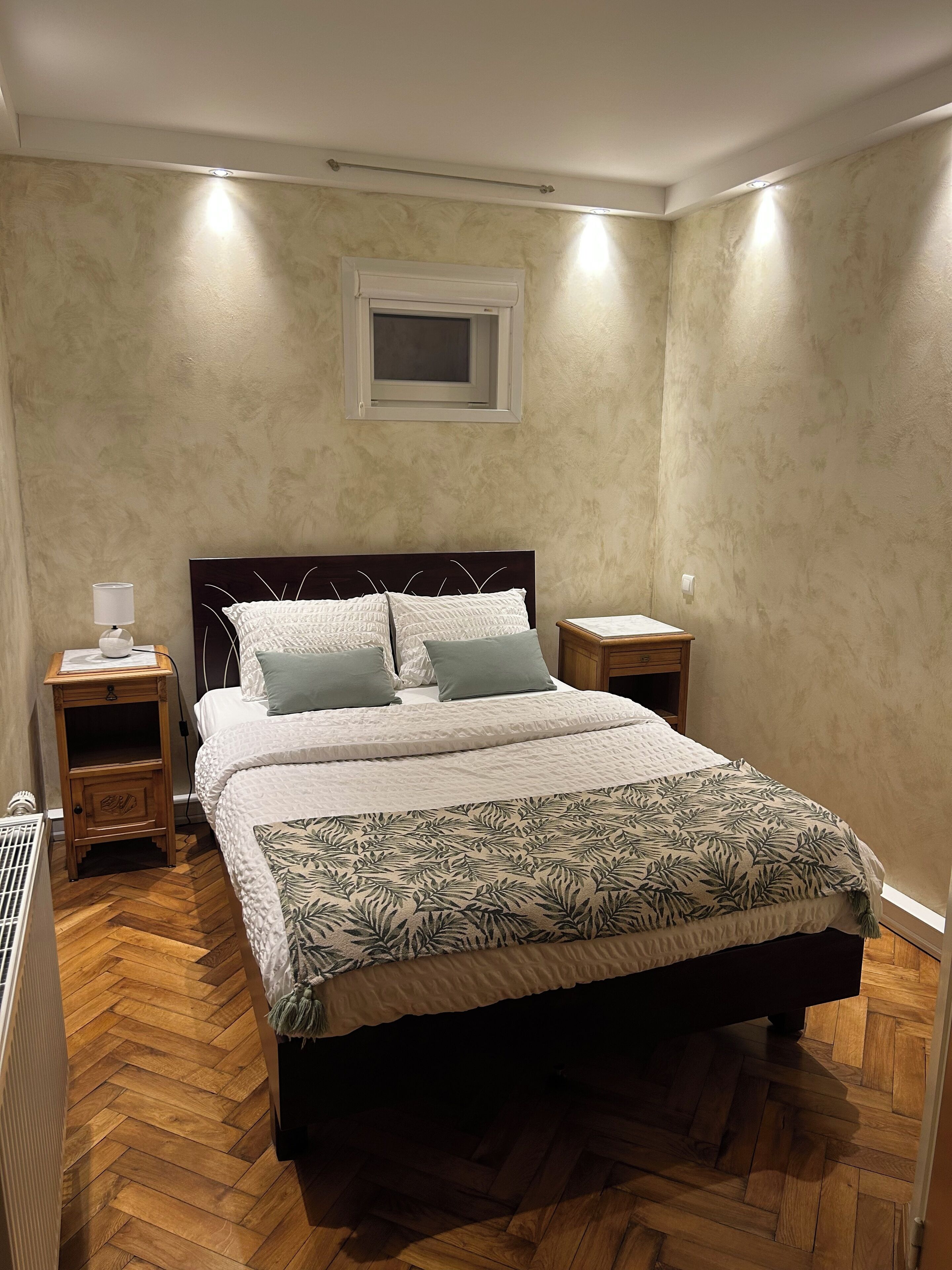 Een slaapkamer met een groot bed, twee nachtkastjes, een radiator en een raam met zonwering.