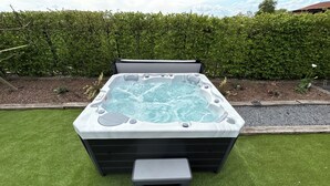 A hot tub with a step and a control panel, surrounded by a well-maintained lawn and a hedge. - La Ferme du Paradis (Merris)